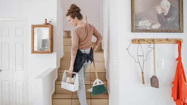Eine Frau mit Putzutensilien und Besen geht eine Treppe hinauf, bereit für den Frühjahrsputz.