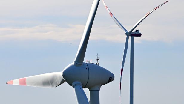 Zwei Windräder mit rot markierten Spitzen stehen vor einem hellen Himmel.