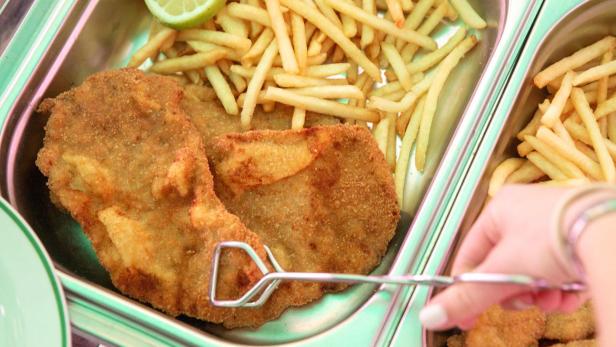 In einer Metallschale liegen Schnitzel, Pommes und eine Zitronenscheibe.