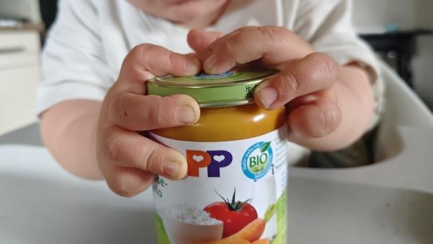 Ein Kleinkind versucht, ein Glas mit Babynahrung mit beiden Händen zu öffnen.