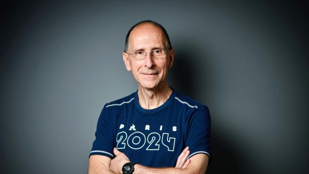 Peter Filzmaier steht in einem Sportleiberl vor grauem Hintergrund