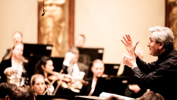 Ein Dirigent leitet ein Orchester, dessen Musiker konzentriert ihre Instrumente spielen.