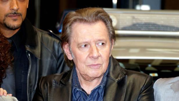 Jan Fedder mit verschränkten Armen in Jeans und Lederjacke, umgeben von anderen Personen, vermutlich bei einer Veranstaltung.