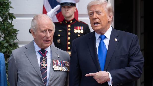 Donald Trump gestikuliert neben König Charles III., während ein Soldat im Hintergrund salutiert.