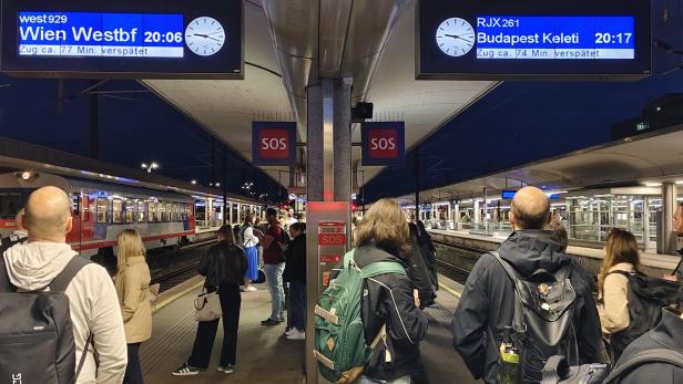 Bahnsteig in Linz mit Anzeigen und wartenden Fahrgästen.