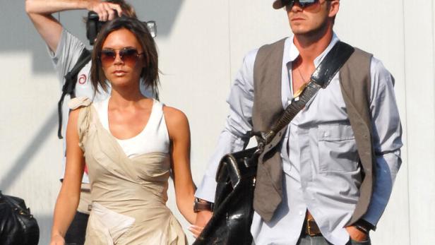  David und Victoria Beckham gehen Hand in Hand an einem sonnigen Tag.. Sie trägt ein Kleid und große Sonnenbrillen, er Stone-Washed-Jeans, Hemd, Gilet, Kappe und große Brille