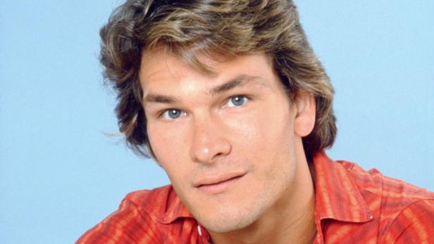 Patrick Swayze, der für seine Rolle in "Ghost – Nachricht von Sam" kämpfen musste, mit verschränkten Armen vor blauem Hintergrund.