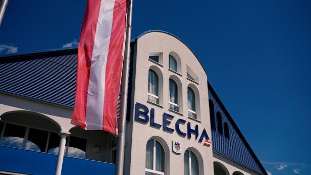 Firmengebäude mit BLECHA-Schriftzug und österreichischer Flagge vor blauem Himmel.