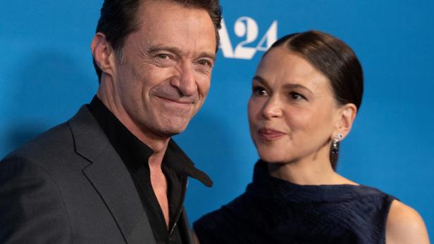 Hugh Jackman und Sutton Foster posieren gemeinsam vor einem blauen A24-Hintergrund.