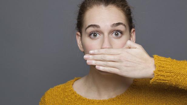 stunned young woman covering her mouth for silence