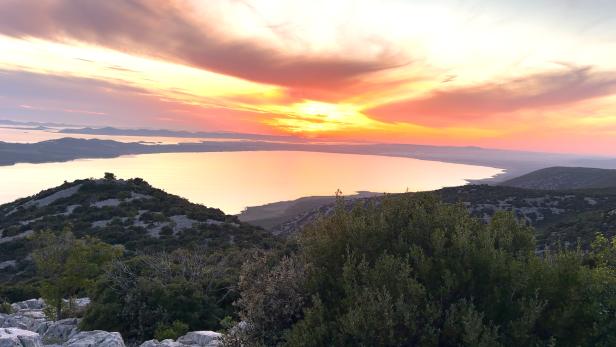 Sonnenuntergang über einer kroatischen Küstenlandschaft mit Meer und Hügeln.