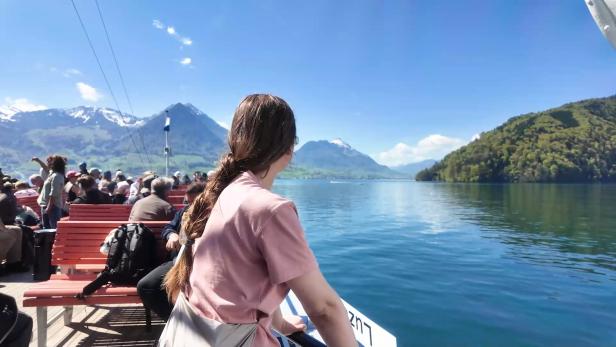 Eine Frau blickt vom Deck eines Ausflugsschiffs auf den Vierwaldstättersee und die Schweizer Berge.