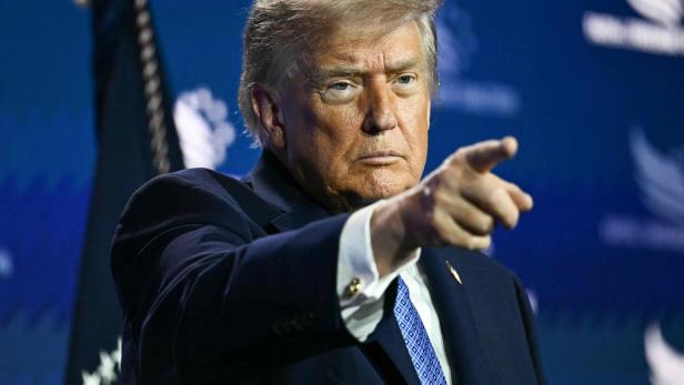Donald Trump zeigt mit ernstem Blick und ausgestrecktem Finger in eine Richtung.