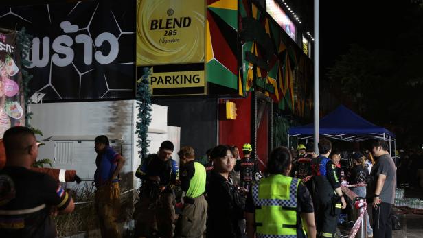 Nachts stehen Feuerwehrleute und Helfer vor einem beleuchteten Gebäude mit „BLEND 285“ und „PARKING“.