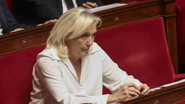 Marine Le Pen sitzt in einem weißen Hemd auf einem roten Sitzplatz in der französischen Nationalversammlung.