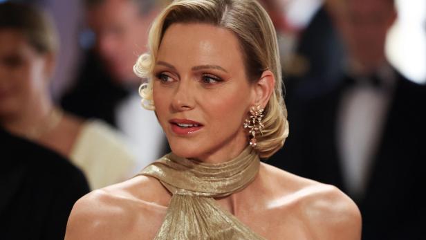 Fürstin Charlène von Monaco trägt ein goldenes Kleid und elegante Ohrringe bei einer formellen Veranstaltung.