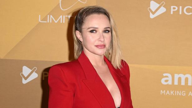 Hayden Panettiere trägt einen roten Blazer vor einem goldfarbenen Hintergrund mit amfAR-Logos.