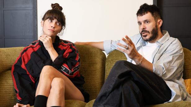 Noga Erez und Ori Rousso sitzen auf einem Sofa und sprechen miteinander, der Mann gestikuliert.