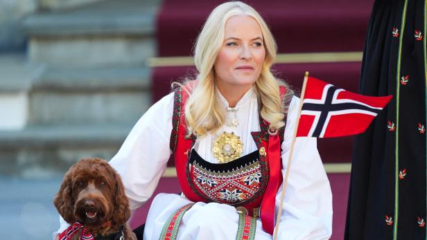 Königin Mette-Marit von Norwegen trägt eine traditionelle Tracht und hält eine norwegische Flagge neben ihrem Hund.