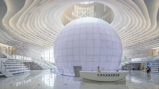 Die futuristische Tianjin Binhai New Area Library besticht durch geschwungene Bücherregale und eine zentrale, leuchtende Kugel in der Mitte.