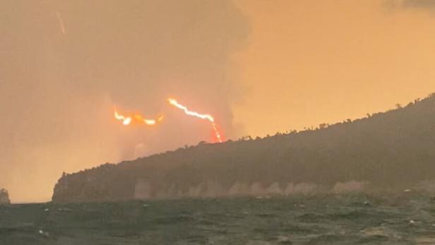 Blitze zucken über einer Küstenlandschaft bei dunklem Meer.
