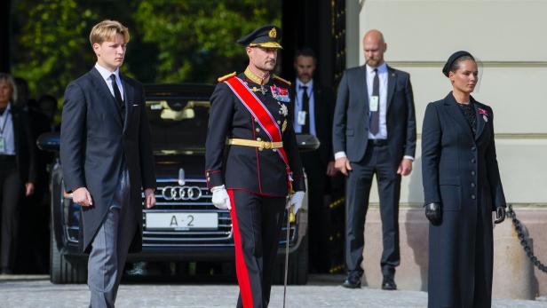 Prinz Sverre Magnus, König Haakon in Uniform und Prinzessin Ingrid Alexandra schreiten vor einem Audi mit dem Kennzeichen A-2 feierlich voran.