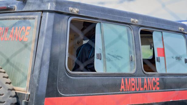 Abgenutzter Krankenwagen mit roter „AMBULANCE“-Aufschrift, darin sitzt eine Person hinter dem Fenster.