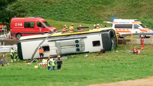 Umgekippter Bus auf einer Wiese, umgeben von Feuerwehr, Rettungskräften und zwei Einsatzfahrzeugen.