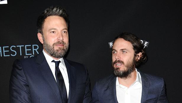 Ben und Casey Affleck bei einer gemeinsamen Premiere in dunklen Anzügen vor einer Fotowand.