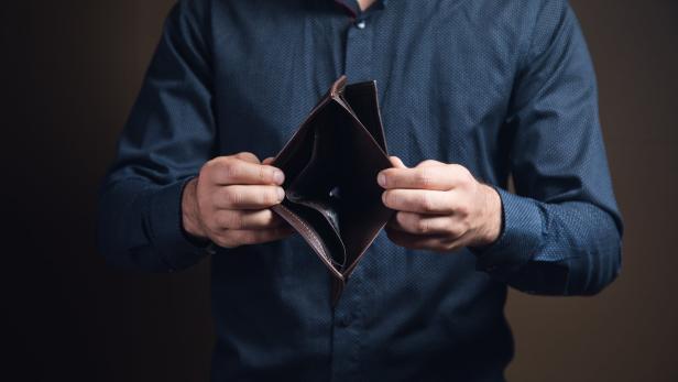 Mann hält ein leeres, offenes Portemonnaie in den Händen.