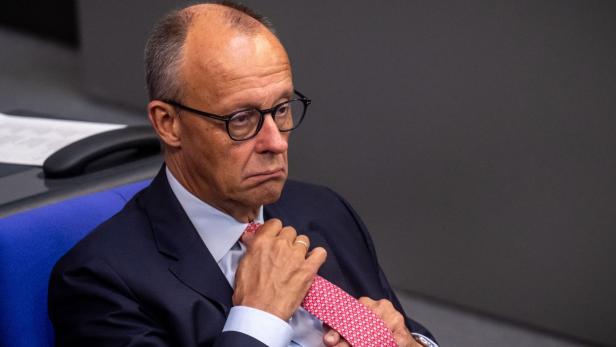 Ein ernst blickender Mann im Anzug richtet seine rote Krawatte.