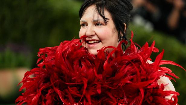  Lena Dunham lächelt in einem roten Kleid mit auffälliger Federboa.