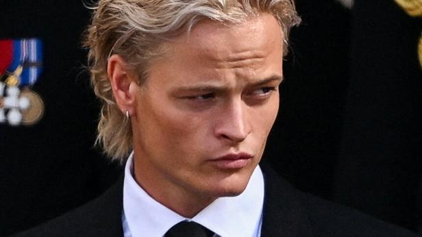 Marius Borg Høiby mit blondem Haar trägt einen schwarzen Anzug mit weißem Hemd und Krawatte.
