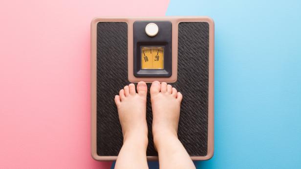 Baby barefoot standing on weight scales on light pink blue floor background. Pastel color. Closeup. Care about body. Children weight control concept. Top down view. Two sides.