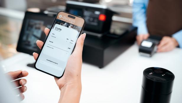 Close-up customer's hand holding a smartphone over a payment terminal E-receipt to complete
