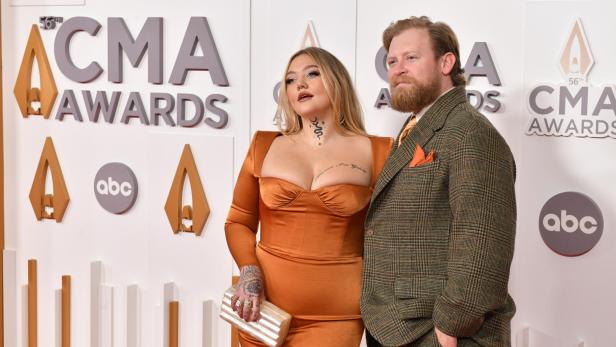 Elle King in einem orangenen Kleid posiert neben ihrem Partner Dan Tooker