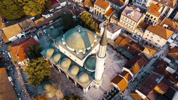 Luftaufnahme einer Moschee mit Kuppeln und Minarett inmitten eng bebauter Altstadt.