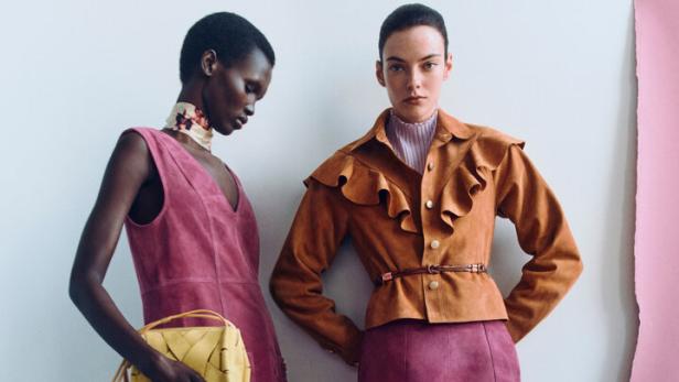 Zwei Models in farbigen Mode-Outfits posieren vor einer hellen Wand.