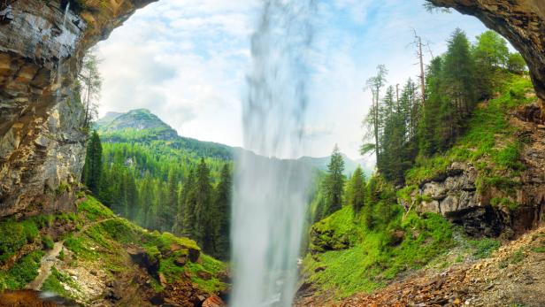 View through a waterfall into a valley with forests and mountains - johannes waterfall, Austria Alps mountain