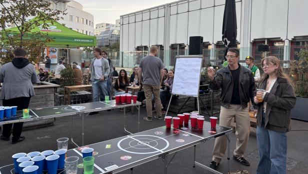 Eine Gruppe junger Leute spielt Beer Pong an mehreren Tischen.