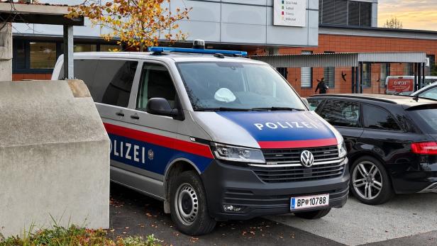 Polizeiwagen vor einem modernen Schulgebäude mit Herbstbäumen.