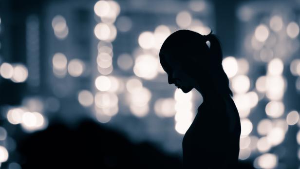 Silhouette einer Frau im Profil vor unscharfen Stadtlichtern bei Nacht.