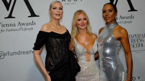 Drei elegant gekleidete Frauen posieren vor einer Sponsorenwand bei den Vienna Awards.