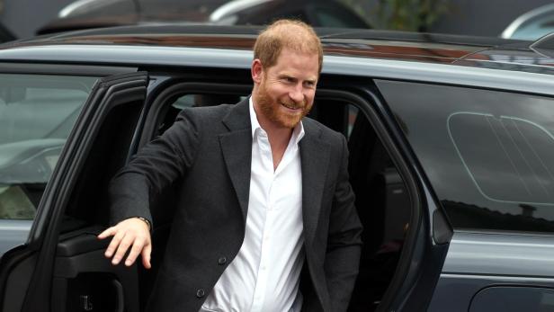 Prinz Harry steigt lächelnd aus einem dunklen Auto.