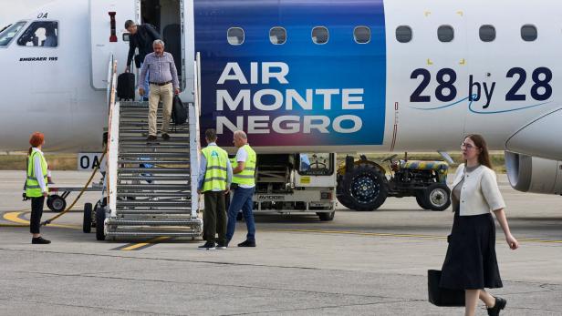 Passagiere verlassen ein Flugzeug der Fluggesellschaft Air Montenegro über eine mobile Treppe auf einem Rollfeld.