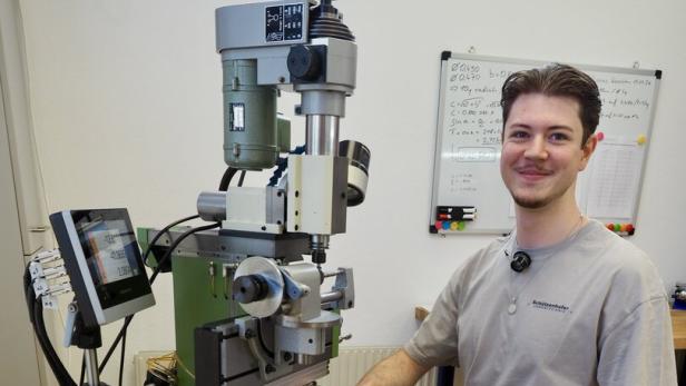 Ein junger Mann sitzt neben einer großen Fräsmaschine in einer Werkstatt.