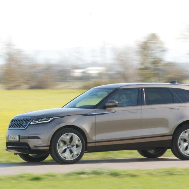 Ein goldfarbener Range Rover Velar fährt auf einer Landstraße.
