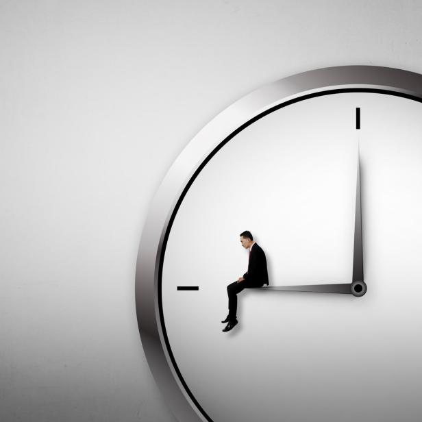 Ein Mann im Anzug sitzt auf dem Zeiger einer großen Uhr.