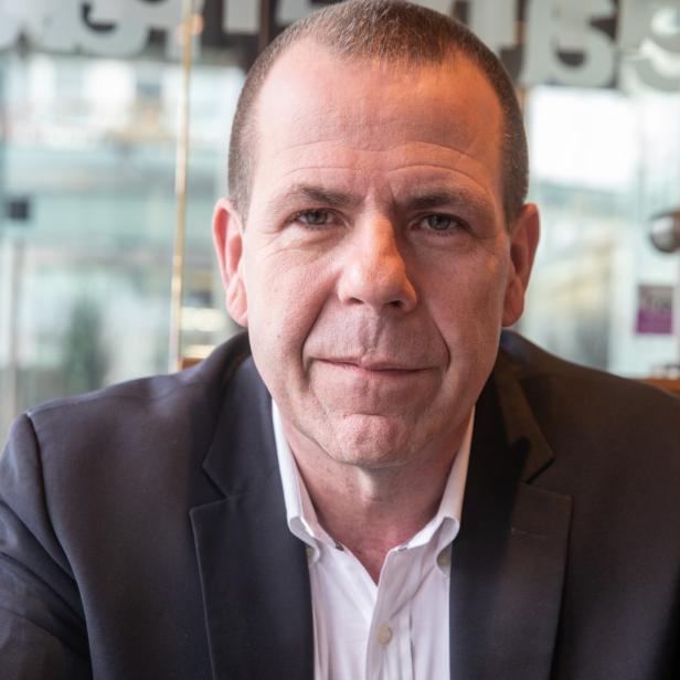 Ein Mann in einem dunklen Anzug blickt in die Kamera.