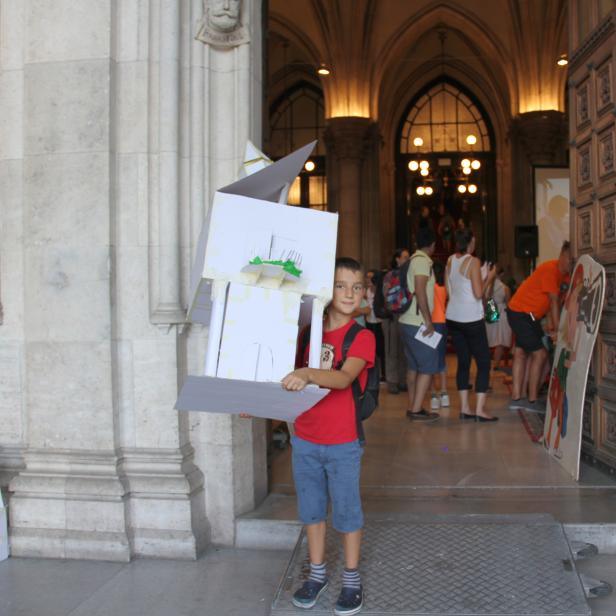 Ein Junge hält ein Architekturmodell aus Pappe vor dem Wiener Rathaus.